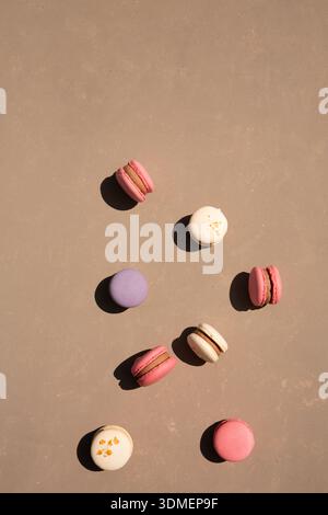 Köstliche bunte Dessert-Makronen mit Füllung auf beigefarbenem Hintergrund mit Sonnenstrahlen, Blick von oben Stockfoto
