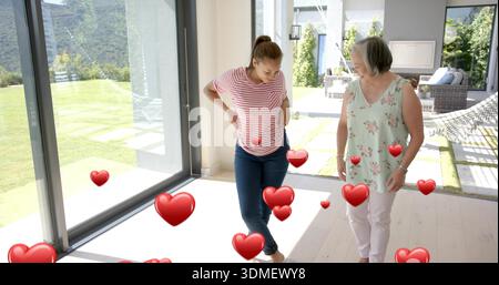 Lächelnde Frau in Blumenoberteil, die Teenager in gestreiftem Oberteil neben Glasschiebetüren umarmt, mit Herzen Stockfoto