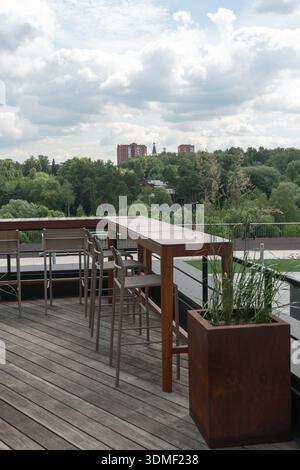 Moskau, Russland - 28. Juni 2025: Außenterrasse mit Holztischen und Blick auf den grünen Park in Skolkovo Stockfoto