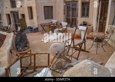 Unordentliche Terrassenmöbel, Klappstühle und ein gefallener Sonnenschirm auf einer Terrasse in Oia, Santorin, Griechenland. Reiseunterbrechung, Sturmschaden hinten Stockfoto