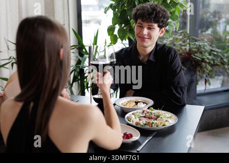 Ein Paar toast Rotwein während eines intimen Abendessens in einem modernen Restaurant. Geeignet für Hospitality, Dating und Lifestyle Marketing Visuals. Stockfoto