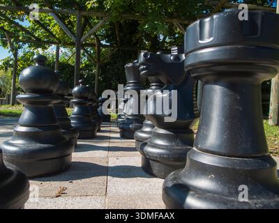 Flacher Blick aus der Witwenperspektive auf Schachfiguren, die für ein Freiluftspiel unter einer Pergola aufgestellt wurden. Stockfoto