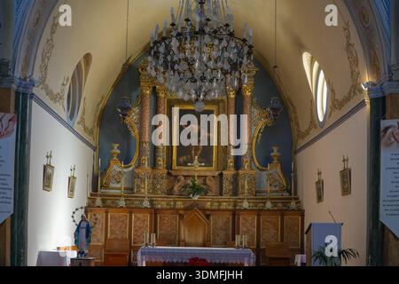 Heilige Kathedrale des Heiligen Johannes des Täufers, katholisches Kircheninnere in Fira, Santorin, Griechenland. Verfügt über einen kunstvollen Retablo-Altar und Kronleuchter. Stockfoto