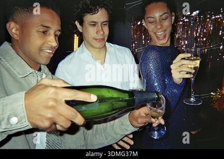 Eine Gruppe von Freunden feiert ein freudiges Ereignis, lächelt und lacht während einer Party, während sie Champagner in Gläser gießt, was ein festliches und festliches Ereignis schafft Stockfoto