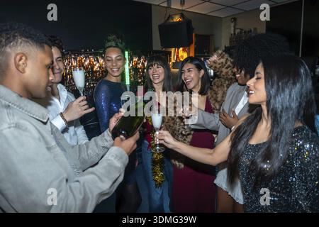 Eine junge Gruppe von Freunden, die einen besonderen Anlass in einem Nachtclub feiern, Champagner in Gläser gießen und einen Toast machen und die Party im genießen Stockfoto