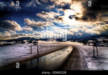 Winterstraße schlängelt sich durch verschneite Landschaft unter dramatischem Himmel, Winter, verschneite Landschaft, Passauer Land, Passau, Niederbayern, Bayern Deutschland Stockfoto