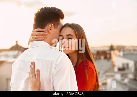 Ein Paar steht ganz in der Nähe auf einem Dach und genießt den Sonnenuntergang, während es sich umgibt. Sie teilen einen ruhigen Moment in der Stadt. Stockfoto