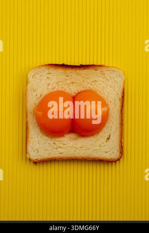 Ei aus zwei Eigelb und geröstetem Brot auf gelbem Hintergrund. Flache Lagen. Osterkonzept. Stockfoto