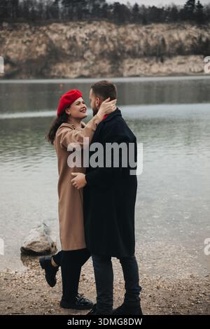 Zwei Personen genießen einen kurzen Moment am Wasser. Sie lächeln, während sie sich in der Nähe einer malerischen Küste umarmen. Stockfoto