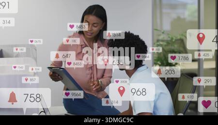Eine Kollegin, die ein Tablet in rosa Bluse hält, Jeans im Büro mit Social Overlays Stockfoto