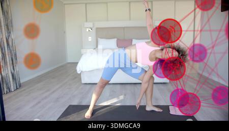 Eine Erwachsene Frau, die sich auf der Yoga-Matte im Schlafzimmer beugt, trägt rosa BH blaue Shorts, grafische Überzüge Stockfoto
