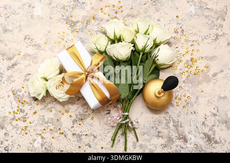 Komposition mit Geschenkbox, Flasche Parfüm und weißen Rosenblüten auf beigem Grunge-Hintergrund Stockfoto