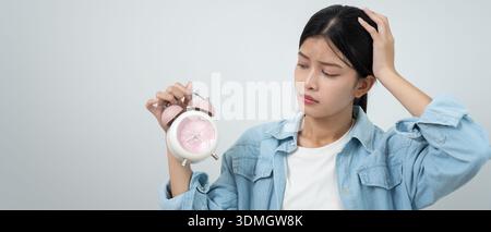 Schockierte junge asiatische Frau, die auf den Wecker schaut, Dame ist zu spät Termin oder Arbeit oder Unterricht, verschlafen, Schwierigkeiten morgens aufzustehen, Zeit besorgt Stockfoto