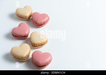 Sechs herzförmige Macarons lagen auf einer weißen Oberfläche. Drei sind rosa und drei sind beige, was ein schlichtes, aber ansprechendes Design darstellt. Stockfoto
