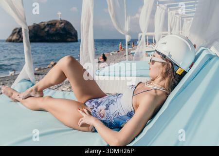 Frau Strandhelm entspannt sich auf blauem Liegestuhl am Meer und repräsentiert einen Bauarbeiter auf Urlaubskonzept Stockfoto