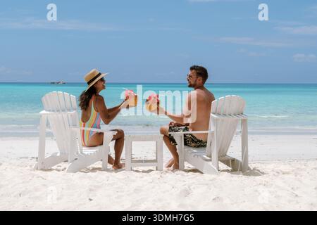 Ein paar entspannen sich auf dem weißen Sand von Grand Anse Beach, Praslin Seychellen und trinken frische Kokosgetränke. Das pulsierende blaue Meer und der klare Himmel sorgen für einen Stockfoto