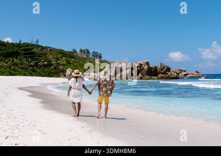 Weißer Sand erstreckt sich entlang des Anse Cocos Strandes, wo ein paar Hand in Hand unter der Sonne spazieren gehen. La Digue Seychellen Stockfoto