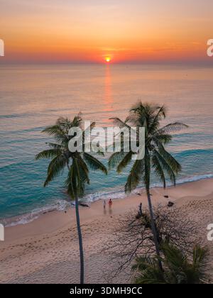 Erleben Sie die ruhige Schönheit des Takhian Beach in Koh Kood, Thailand, während die Sonne über ruhigem Wasser untergeht. Ein paar Männer und eine Frau am Strand in der Sonne Stockfoto