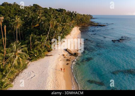 Erleben Sie die Ruhe des Takhian Beach in Koh Kood, Thailand, während zwei Reisende entlang der weichen Sandküste, umgeben von üppigen Palmen und schlendern Stockfoto