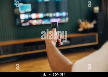 Fokussiertes Foto von der Hand des Mannes, die die Fernbedienung hält, sitzend und in freier Zeit. Stockfoto