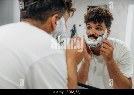 Rasiervorgang. Der Kerl ist im Bad und kümmert sich um sein Aussehen. Stockfoto