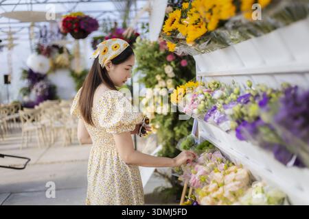Schöne junge asiatische Frau im Blumenladen, in Ruhe einkaufen für bunten Blumenstrauß. Glückliche Frau, die frische Blüten aus dem Blumengeschäft wählt Stockfoto