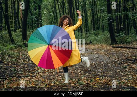 Lauf mit buntem Regenschirm. Junge Frau genießt die Natur im Wald unter dem Regen. Stockfoto