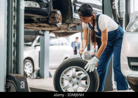 Rollen des Rads. Die Mechanikerin ist mit Reifen in der modernen Autowerkstatt. Stockfoto