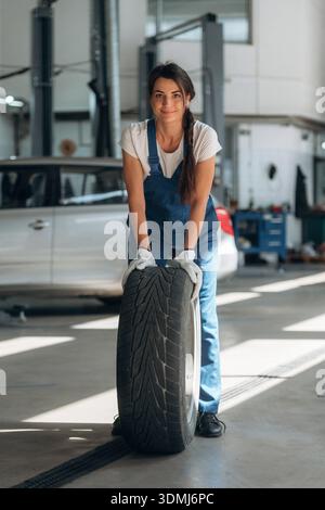 Rollen des Rads. Die Mechanikerin ist mit Reifen in der modernen Autowerkstatt. Stockfoto