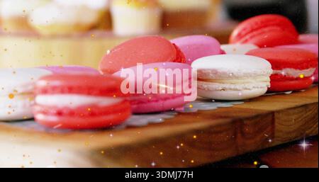 In der Bäckerei werden bunte Macarons auf Holzbrettern präsentiert, mit Papierdeckchen und goldenem Glanz Stockfoto