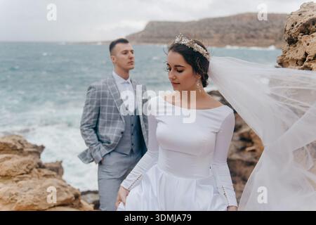 Jungvermählte posieren am Meer an einem felsigen Ufer Stockfoto
