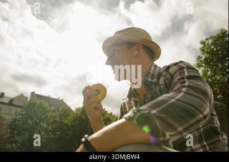 Junger Mann, der einen Apfel genießt, während er sich draußen in der Stadt entspannt. Stockfoto
