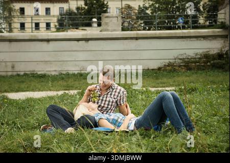 Junge Paare, die sich auf dem Gras im Stadtpark am Fluss in der Stadt entspannen Stockfoto