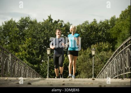 Ein junges Paar, das zusammen auf der Fußgängerbrücke im Park joggt Stockfoto