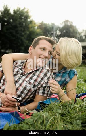 Nahaufnahme eines jungen Paares, das draußen mit Ohrhörern auf dem Gras kuschelt Stockfoto