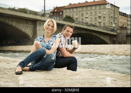 Ein junges Paar, das am Fluss sitzt und gemeinsam Kaffee genießt Stockfoto