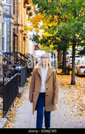 Eine ältere asiatin läuft eine urbane Straße entlang Stockfoto