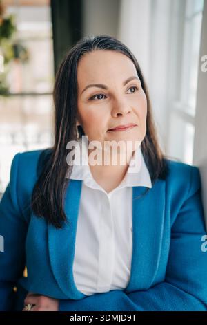 Professionelle Frau in einem blauen Blazer, die nachdenklich aus dem Fenster schaut Stockfoto