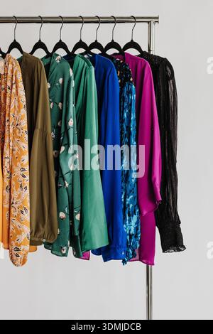 Nahaufnahme der Oberteile für Damen, die in Regenbogenreihenfolge auf dem Rack hängen Stockfoto