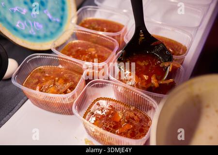 Suppen servieren. Zubereitung von einzelnen Portionen vibrierender Tomatenbrühe in Behältern. Durchsichtige Boxen vorsichtig mit reichhaltigem Gemüse und füllen Stockfoto