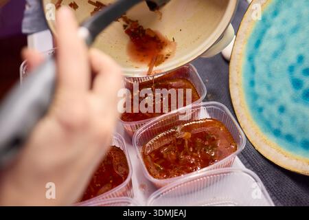 Suppen servieren. Zubereitung von einzelnen Portionen vibrierender Tomatenbrühe in Behältern. Durchsichtige Boxen vorsichtig mit reichhaltigem Gemüse und füllen Stockfoto