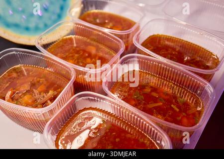 Suppen servieren. Zubereitung von einzelnen Portionen vibrierender Tomatenbrühe in Behältern. Durchsichtige Boxen vorsichtig mit reichhaltigem Gemüse und füllen Stockfoto