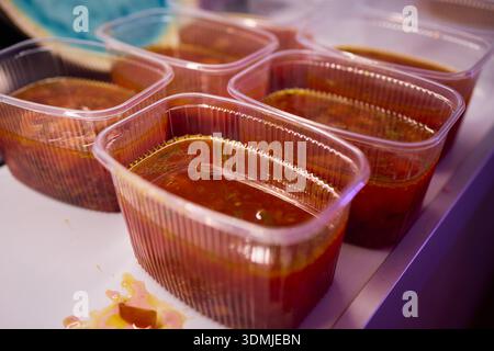 Suppen servieren. Zubereitung von einzelnen Portionen vibrierender Tomatenbrühe in Behältern. Durchsichtige Boxen vorsichtig mit reichhaltigem Gemüse und füllen Stockfoto