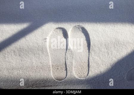 Fußabdrücke in frischem Schnee mit Sonnenlicht-Schatten, die einen abstrakten Winterhintergrund erzeugen Stockfoto