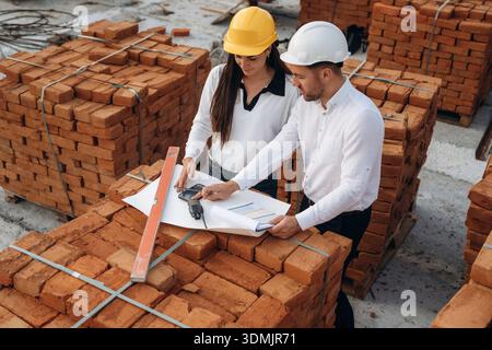 Über den Plan diskutieren, mit Dokumenten. Weibliche Managerin und männlicher Baumeister sind auf der Baustelle. Stockfoto