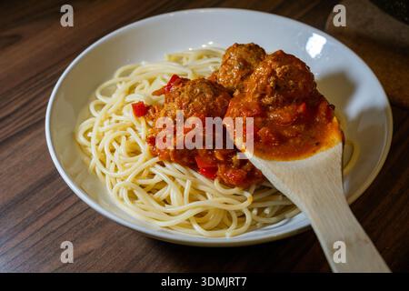 Holzspachtel, in dem Fleischbällchen mit Tomatensoße auf Spaghetti auf einem weißen Teller serviert werden. Stockfoto