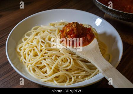 Holzlöffel mit Fleischbällchen mit Tomatensoße über Spaghetti auf einem weißen Teller. Stockfoto