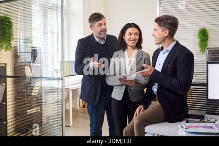 Drei Geschäftsleute sprechen während eines freundlichen Meetings am Schreibtisch über ihre Strategie Stockfoto