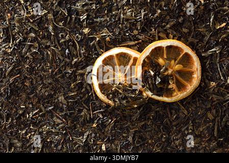 Detail von getrockneten Orangenscheiben auf einem Hintergrund getrockneter Teeblätter. Draufsicht. Stockfoto