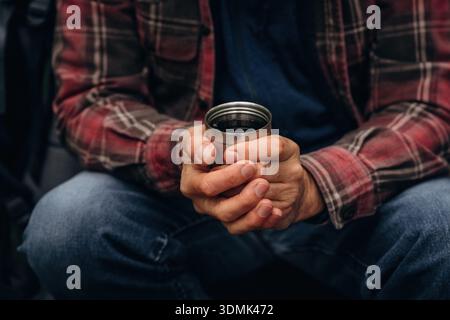 Detaillierte Nahaufnahme eines Mannes, der draußen ist und warmes Getränk in Thermosbecher hält. Stockfoto